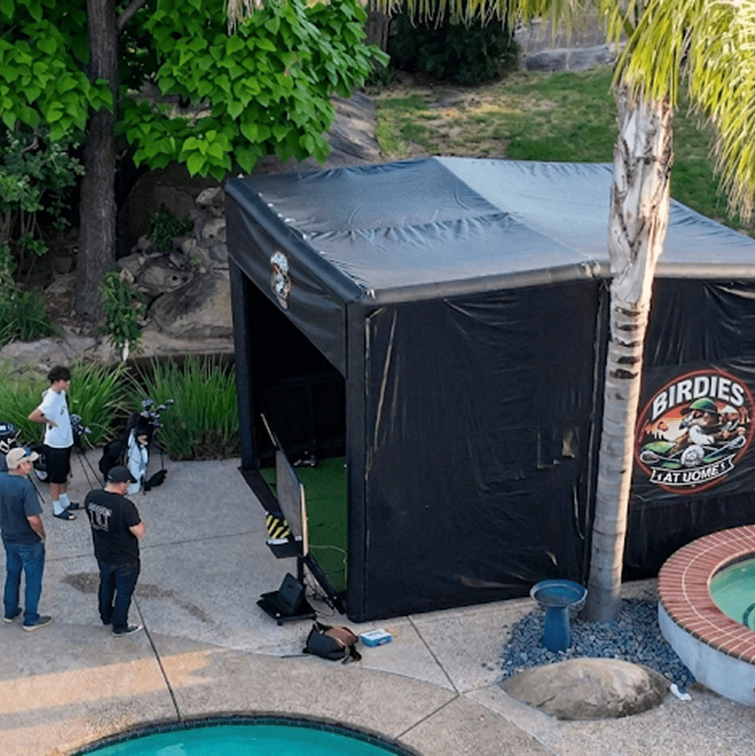 Outdoor golf simulator near pool and trees.